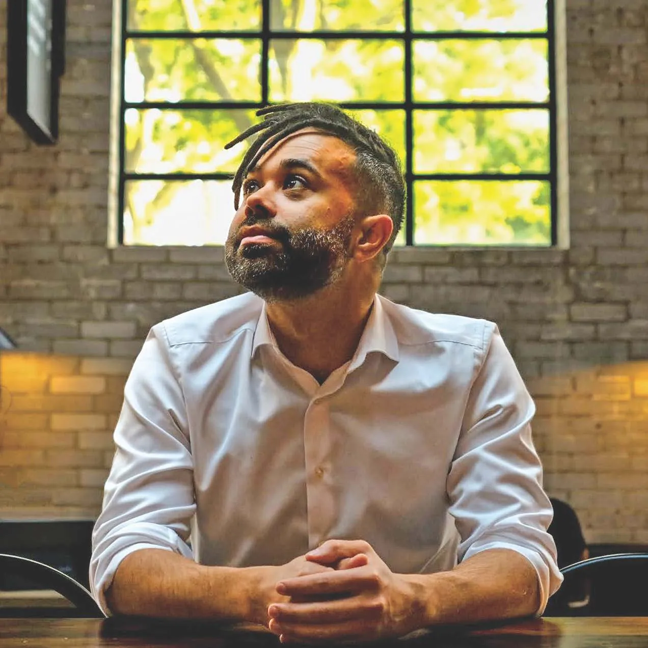 Jordan Loewen-Colón, seated at a wooden table in front of a large industrial window.